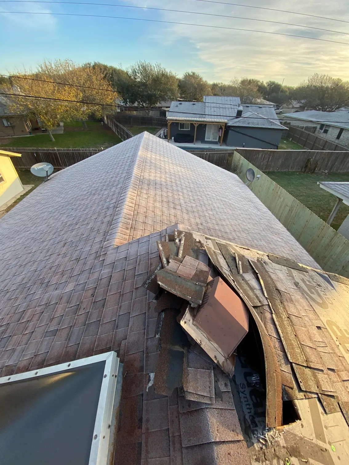 Storm-damaged shingle roof with torn shingles beside a skylight