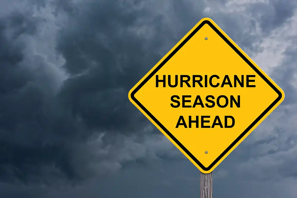 Yellow "Hurricane Season Ahead" road sign under dark storm clouds