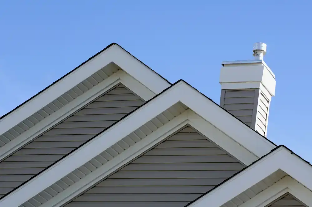Newly installed gray siding on a modern home’s roofline with chimney against a clear blue sky, illustrating enhanced curb appeal and protection.