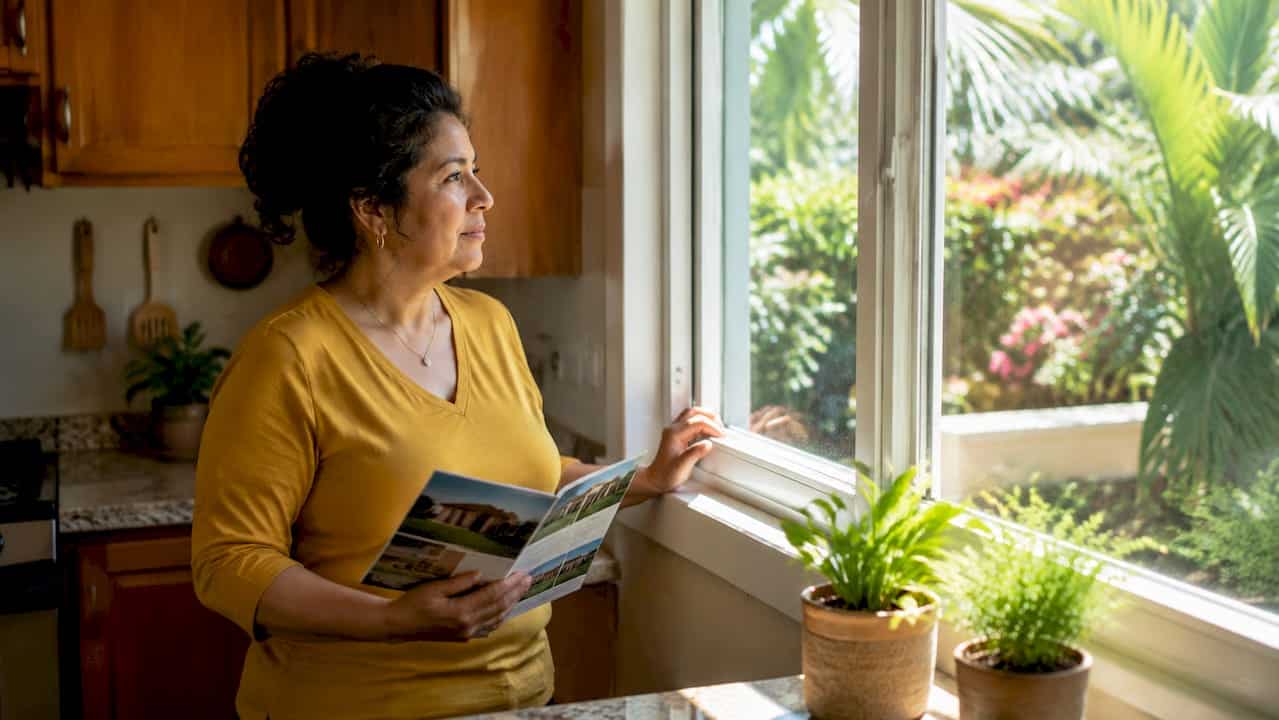 Homeowner inspecting impact-resistant window indoors