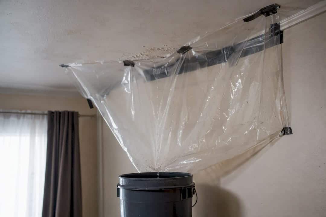 Bucket catching water drip with plastic sheeting indoors